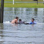 An Australian TV reporter was filming floods when he spotted a sinking four-wheel drive, swam out with a bystander and forced open a rear door to rescue the driver moments before the vehicle disappeared underwater