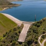 In 1933, California built Santiago Creek Dam to create Irvine Lake; 93 years later, the 750-acre reservoir is being lowered ahead of a five-year project that will drain it entirely before rebuilding key dam structures